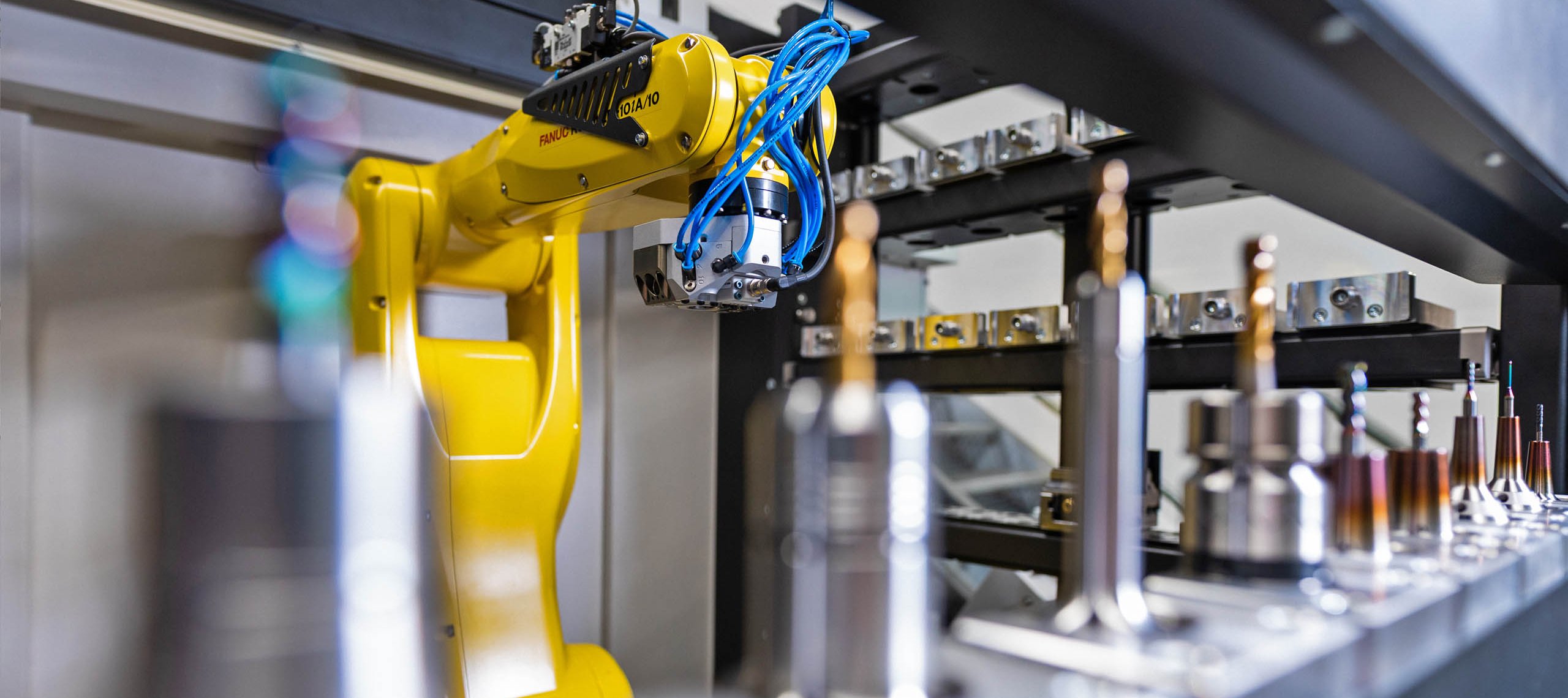 Automation & Robotnik Gelber Industrieroboterarm in Fertigungsanlage mit Metallteilen auf Förderband, Text 'AUTOMATION & ROBOTIK Die RZ-Reihe entlastet Ihre qualifizierten Mitarbeiter'